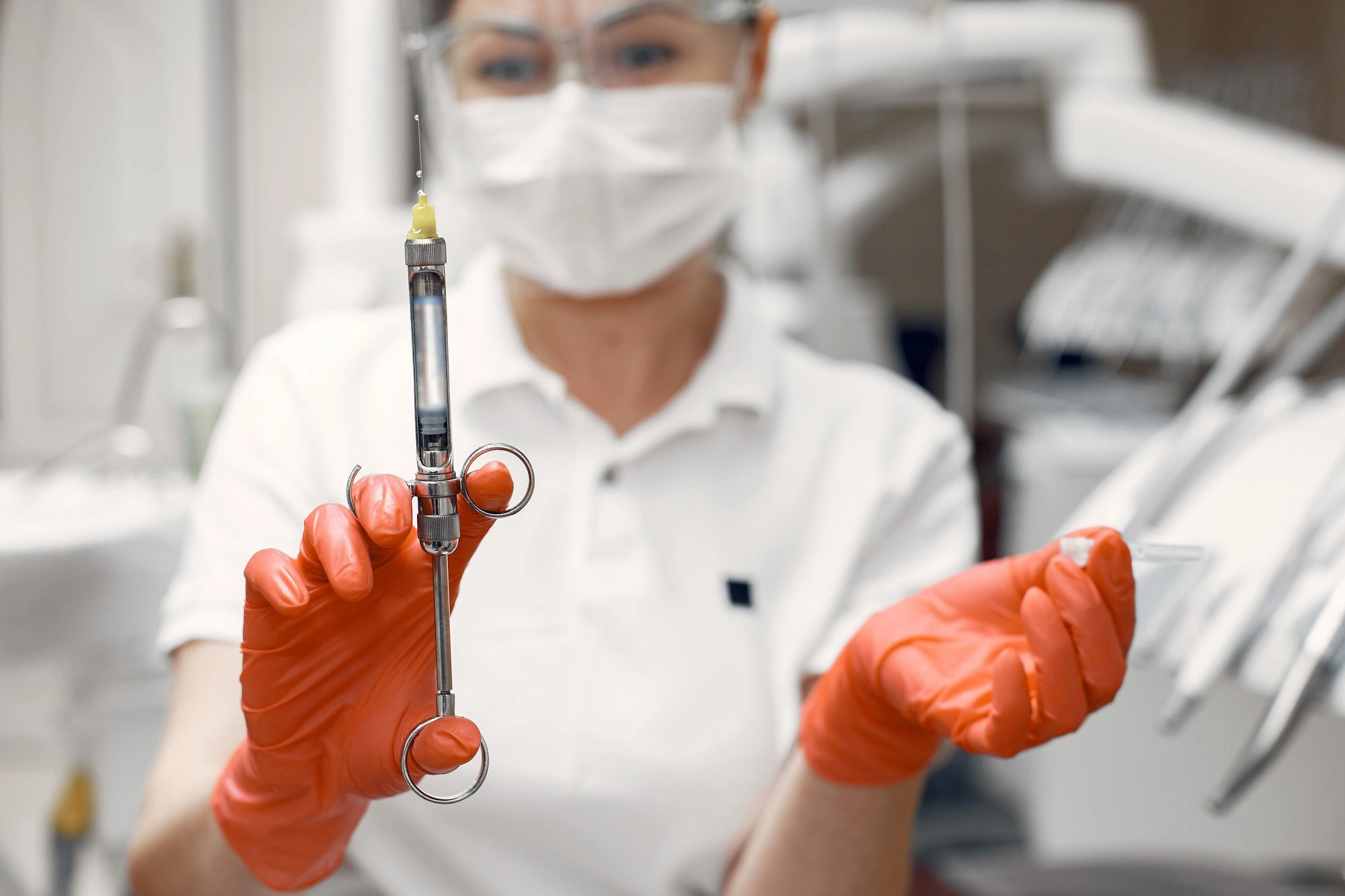 Dentista con guantes naranjas sosteniendo una jeringa para anestesia en una clínica dental, representando la preparación para un procedimiento odontológico